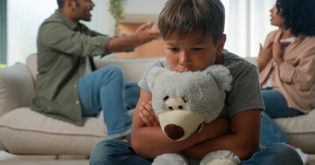 Little boy holding bear while parents argue