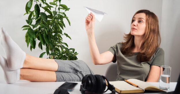 Woman procrastinating at work with paper airplane