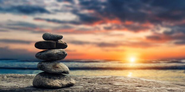 Stack of smooth stones balanced on the beach at sunset with the ocean in the background.